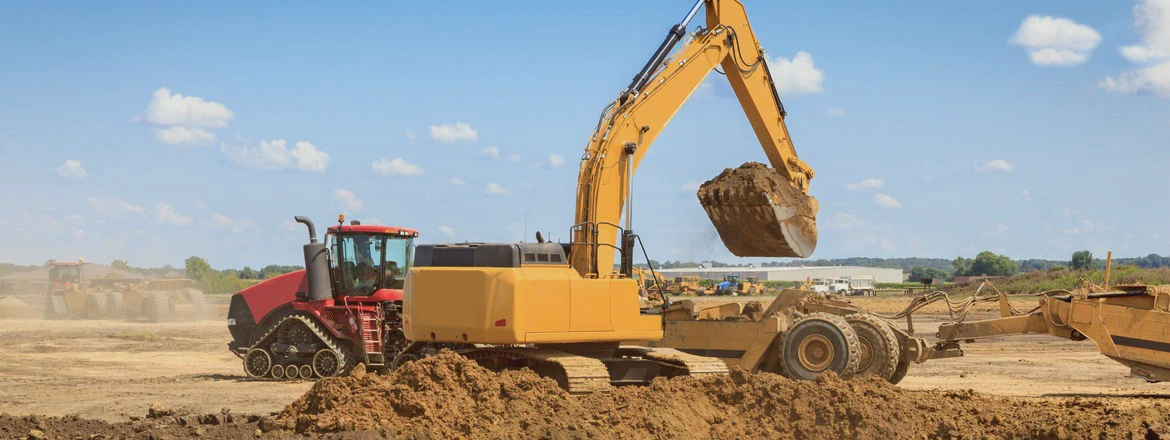 Koparka wykonująca roboty ziemne na&nbsp;placu budowy – wykopy, niwelacja terenu i&nbsp;prace ziemne ciężkim sprzętem